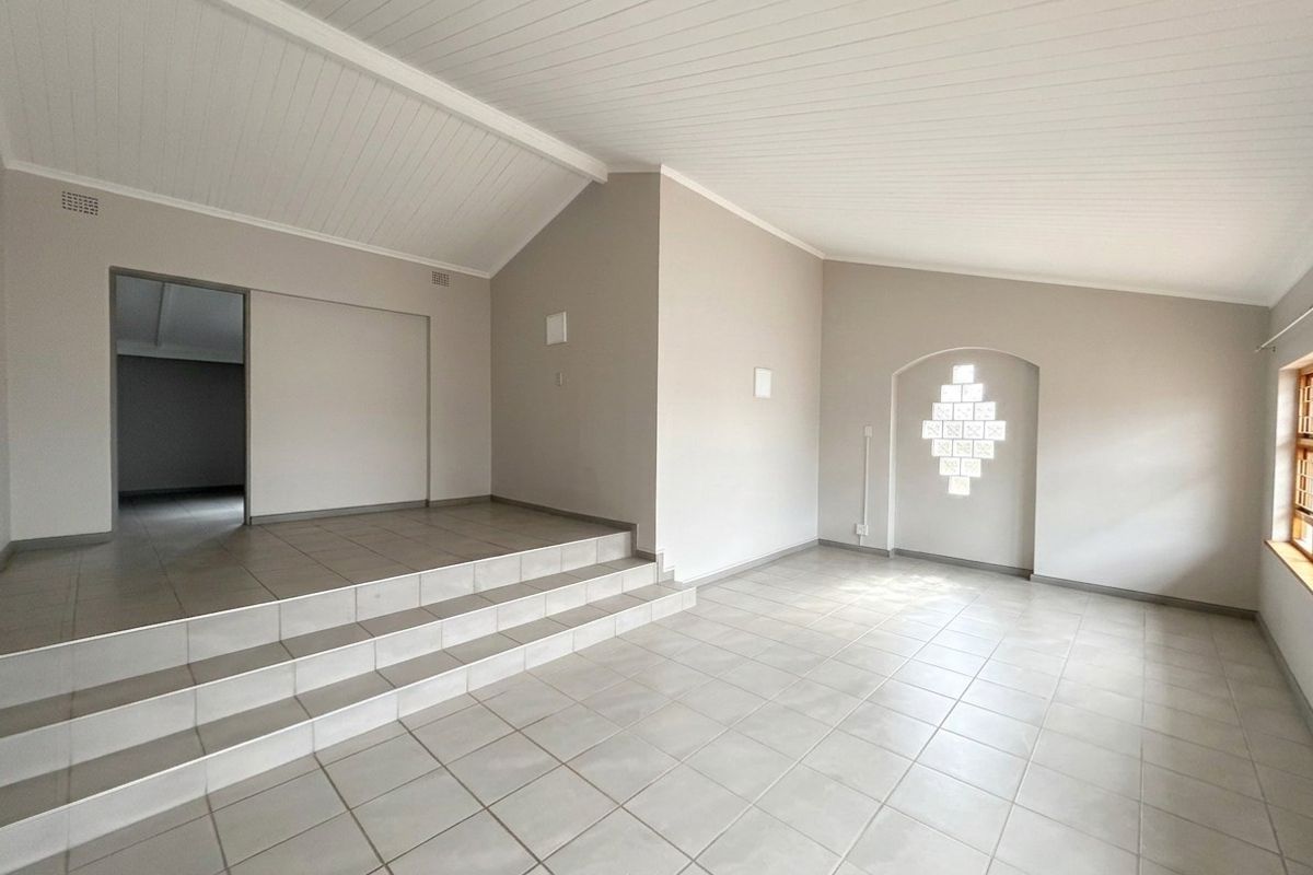 Spacious, light-filled living area featuring a vaulted ceiling, neutral tiled flooring, and a unique glass block feature window with a raised platform section.