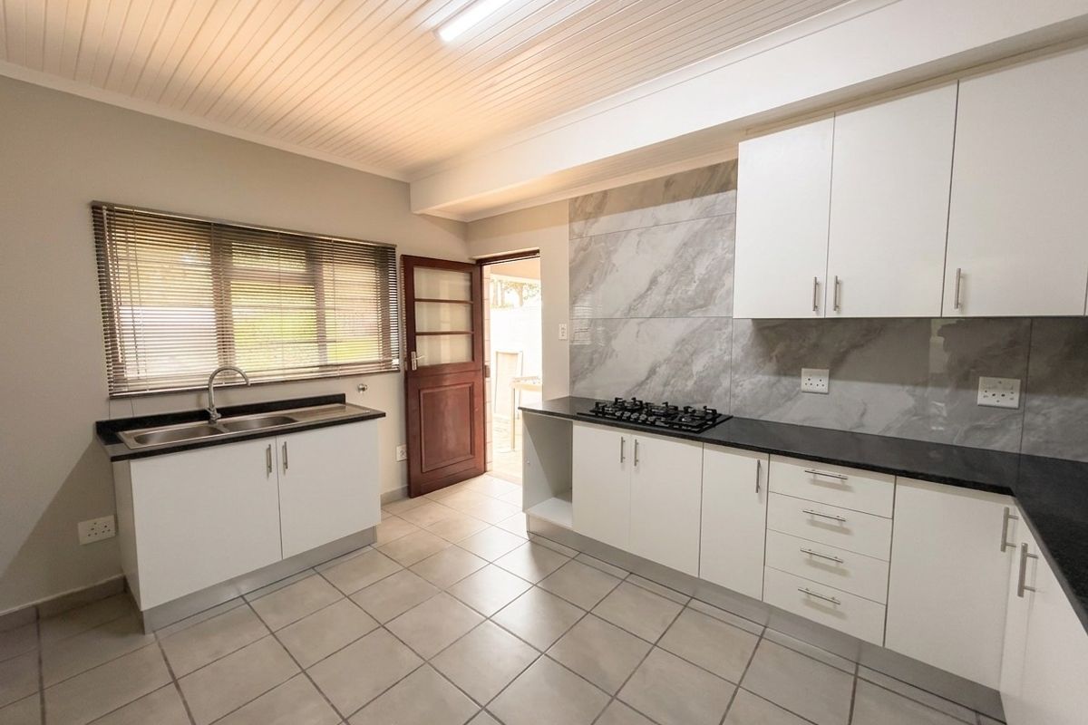 Modern kitchen featuring white cabinetry, stone countertops, gas hob, marble-look splashback, and tiled flooring with direct access to the exterior.