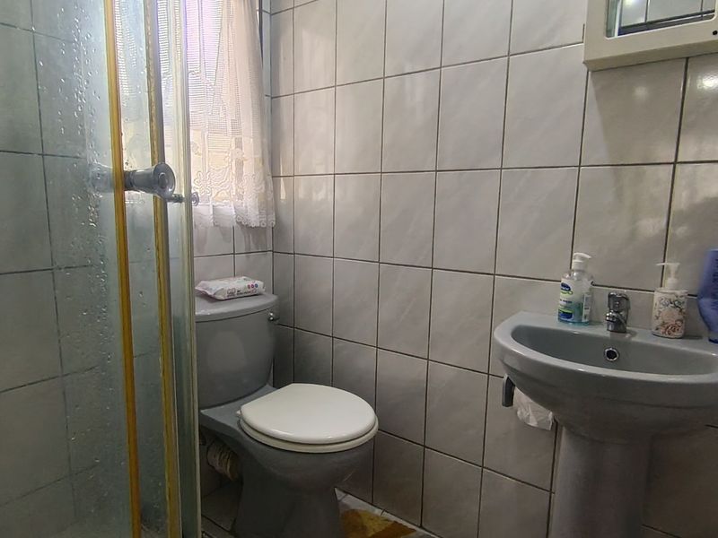A functional bathroom featuring a shower enclosure, pedestal basin, and toilet with full-height wall tiling.