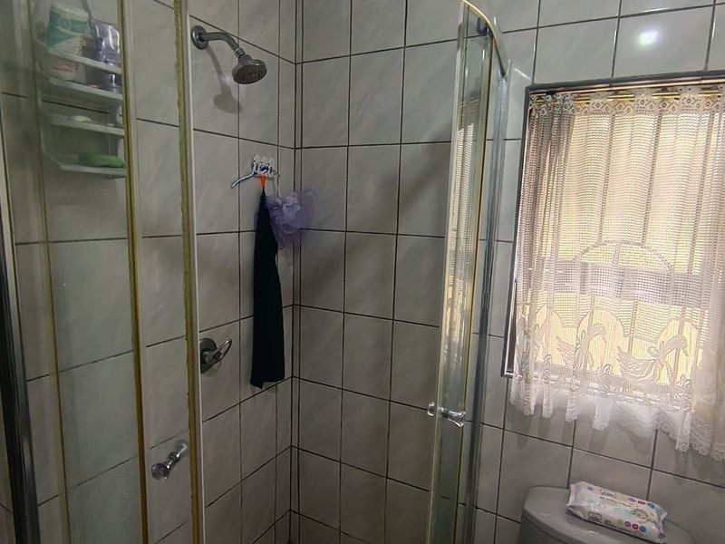 A compact bathroom featuring a shower enclosure with tiled walls and a window with security bars.