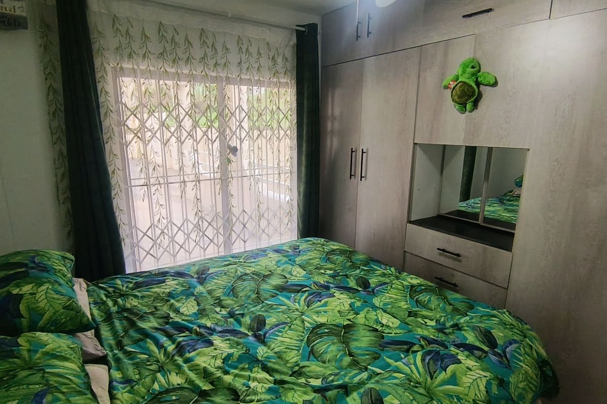 A bedroom featuring built-in cupboards with a central vanity mirror, a ceiling fan, and a sliding door with a security gate leading outside.