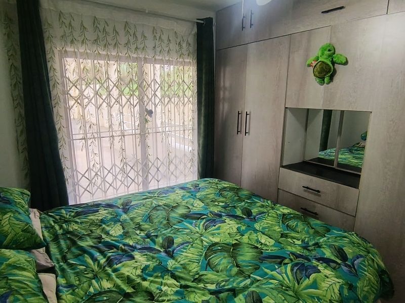 A bedroom featuring built-in cupboards with a central vanity mirror, a ceiling fan, and a sliding door with a security gate leading outside.