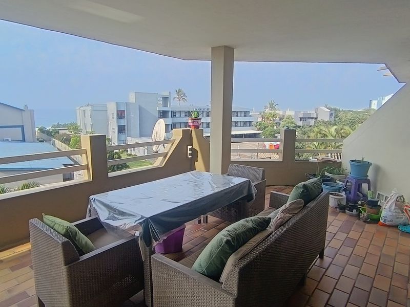 Spacious covered balcony featuring tiled flooring and a concrete balustrade, offering an outdoor living area with views of the surrounding neighborhood.
