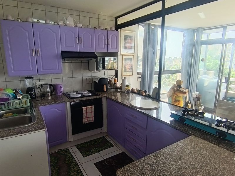 A functional kitchen featuring purple built-in cabinetry, granite countertops, a double basin sink, and an integrated oven with hob, overlooking an adjacent balcony area.