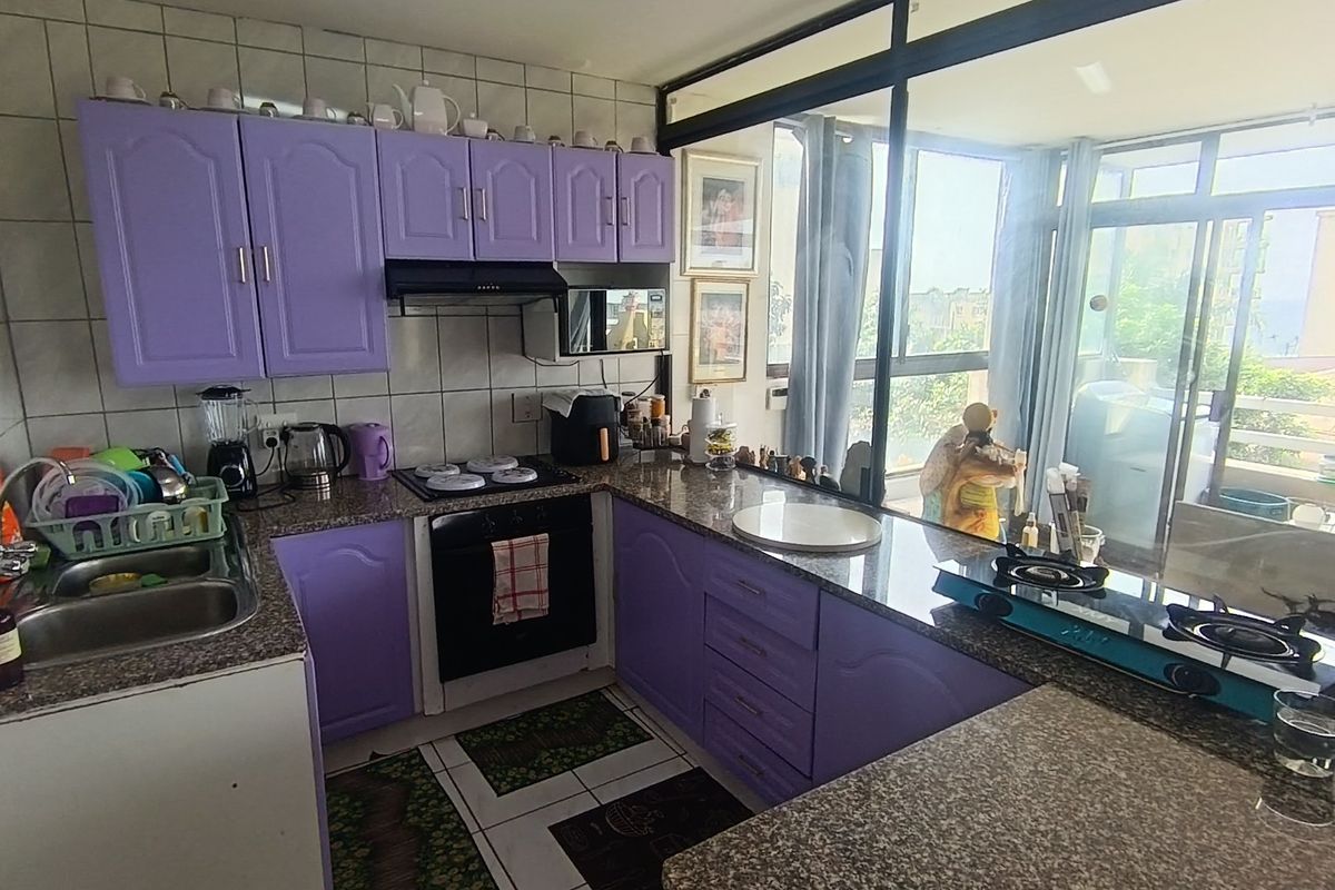 A functional kitchen featuring purple built-in cabinetry, granite countertops, a double basin sink, and an integrated oven with hob, overlooking an adjacent balcony area.