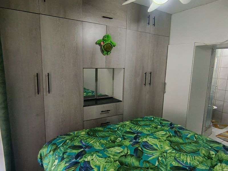 A bedroom featuring extensive built-in cupboards with a central vanity area and an overhead ceiling fan, with an adjoining bathroom visible.