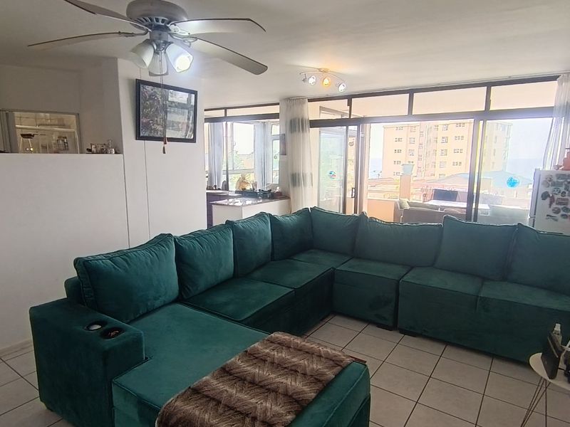 Open-plan living area featuring tiled flooring, a ceiling fan, and large sliding glass doors that provide natural light and access to the balcony.
