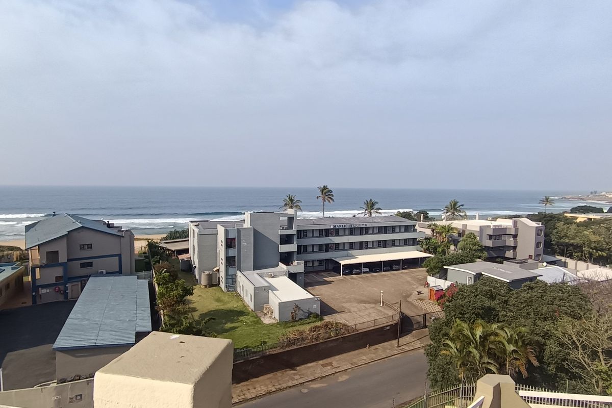 An elevated aerial view of the apartment complex grounds, featuring parking facilities, landscaped areas, and a direct outlook towards the ocean.