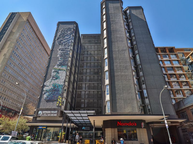 A multi-story commercial building featuring a prominent facade mural, ground floor retail spaces, and a covered entrance canopy in an urban setting.