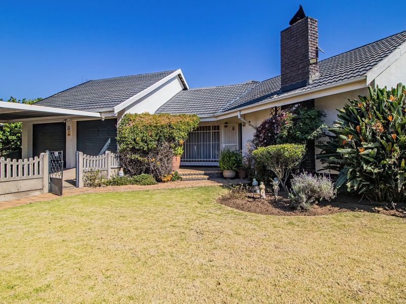 Front elevation of a single-story house featuring a tiled roof, brick chimney, double garage, carport, and a well-maintained front garden with paved access.