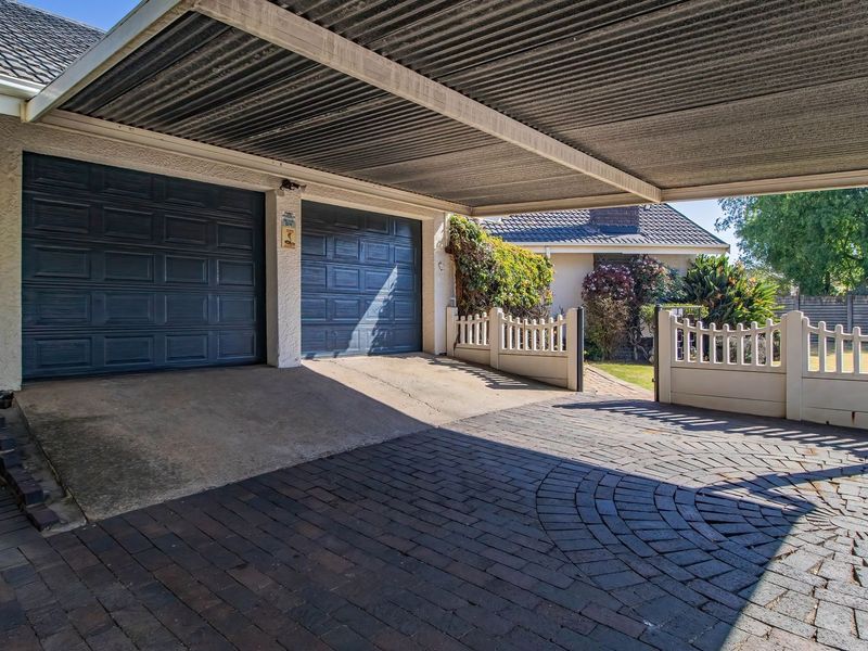 A double garage with a covered carport area and paved driveway, featuring secure boundary fencing and well-maintained exterior structures.