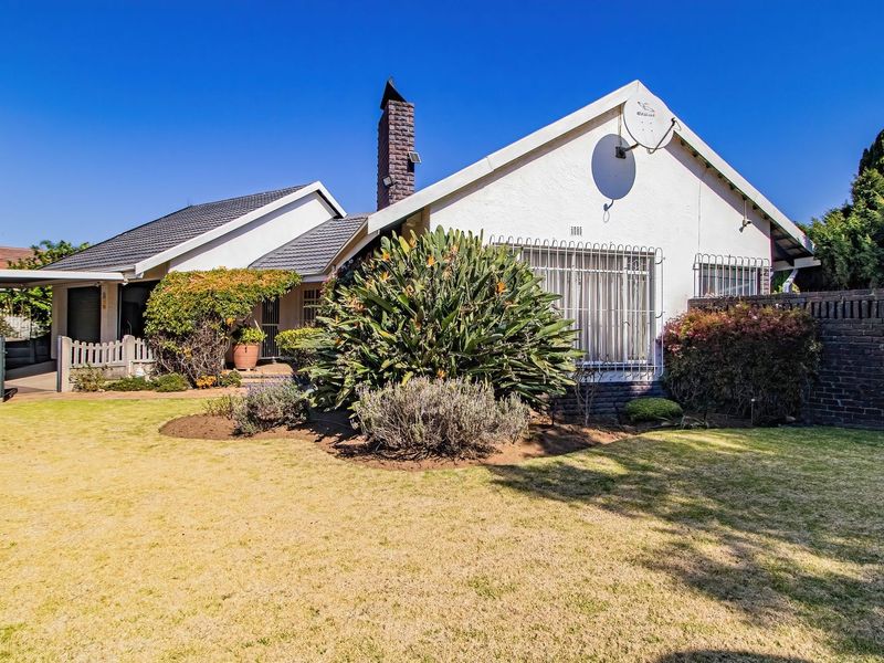 Rear view of a residential house featuring a tiled roof, brick chimney, security bars on windows, and a well-maintained garden area.
