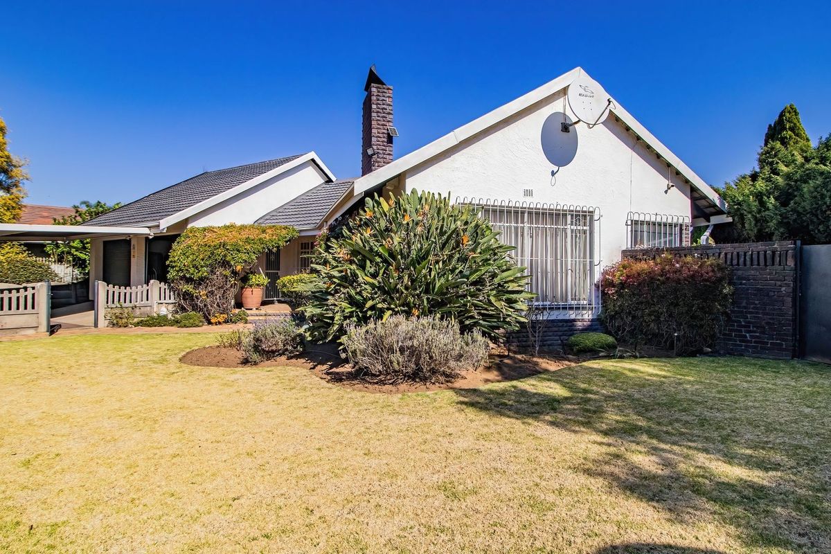 Rear view of a residential house featuring a tiled roof, brick chimney, security bars on windows, and a well-maintained garden area.