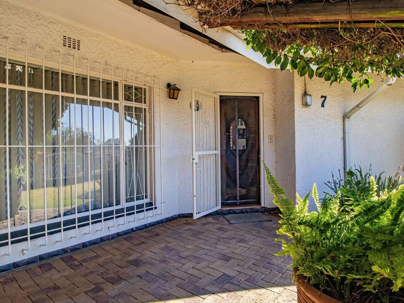 Front entrance area featuring brick paving, a security gate, protective window bars, and a shaded pergola structure.