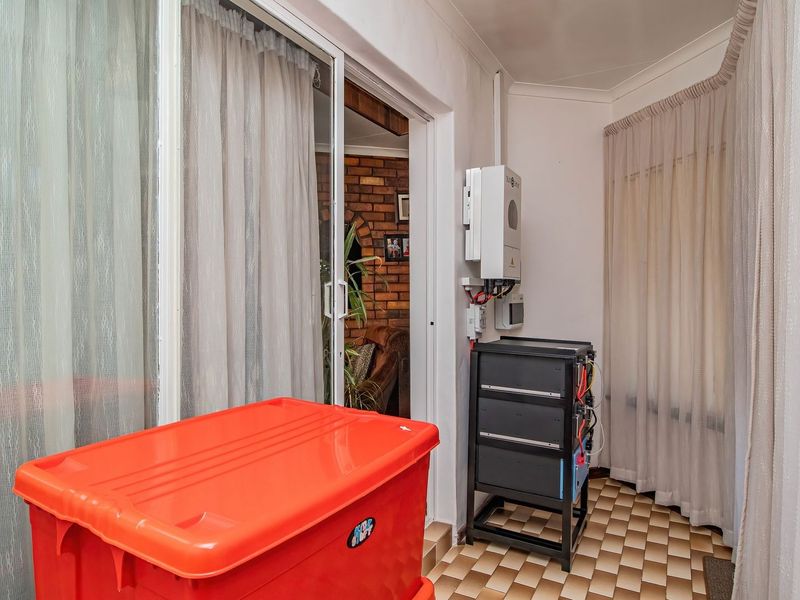 A utility space featuring a wall-mounted inverter and battery storage system, with tiled flooring and access via a sliding glass door.
