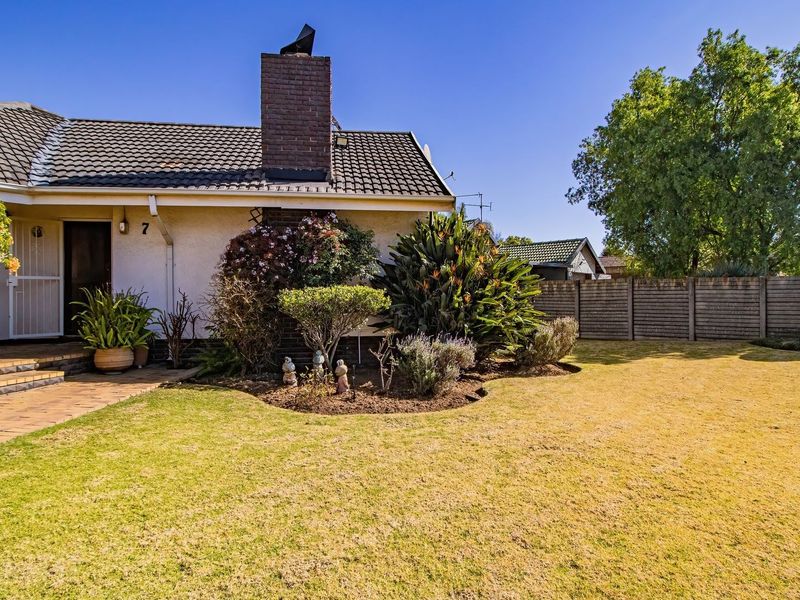 A well-maintained rear garden featuring a paved walkway, established landscaping, and a brick chimney on the exterior facade of the home.