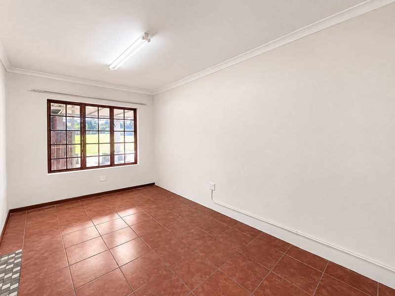 A clean, empty bedroom featuring terracotta floor tiles, a timber-framed window, and neutral walls, ready for personalization.