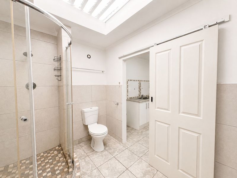 A functional bathroom featuring a shower enclosure, toilet, and tiled finishes, with a sliding door providing access to an adjacent utility area.