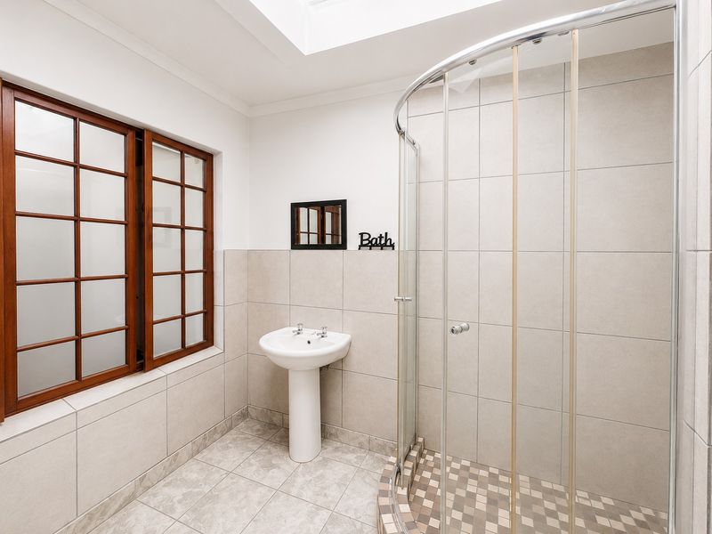 A bright bathroom featuring a pedestal basin, a curved shower enclosure, and a skylight, finished with neutral wall and floor tiling.