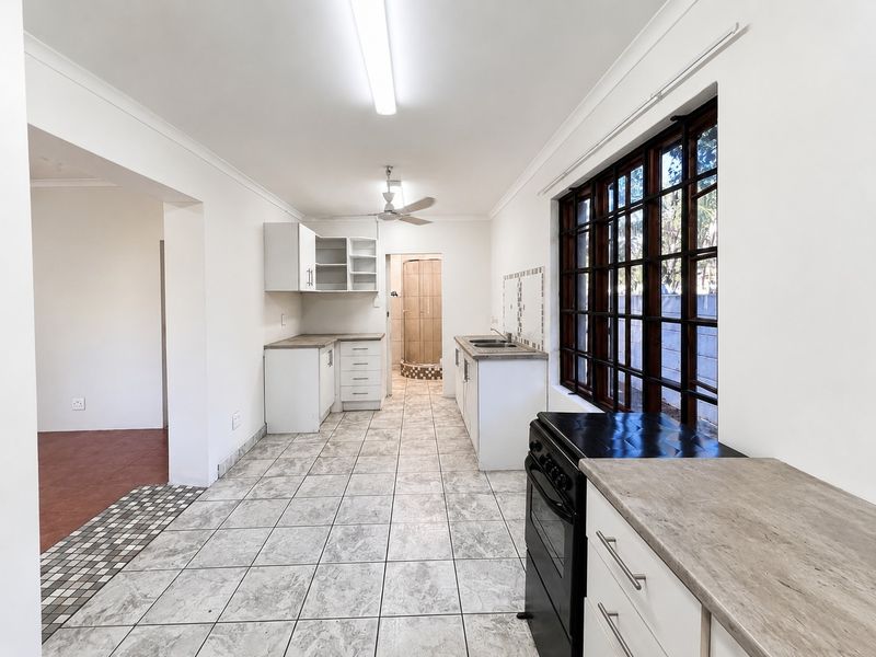 A functional, empty kitchen featuring tiled flooring, laminate countertops, built-in cabinetry, and a large timber-framed window providing natural light.