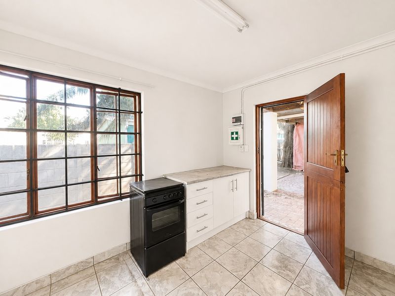 A functional kitchen area featuring tiled flooring, built-in cabinetry with laminate countertops, a freestanding stove, and direct access to an outdoor patio area.