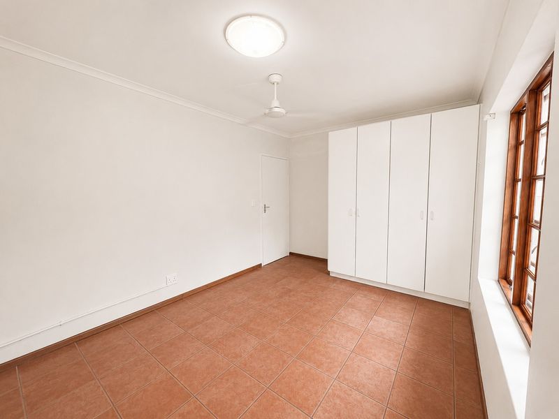 A bright, empty bedroom featuring tiled flooring, built-in cupboards, and a ceiling fan, offering a clean and neutral space ready for personalization.