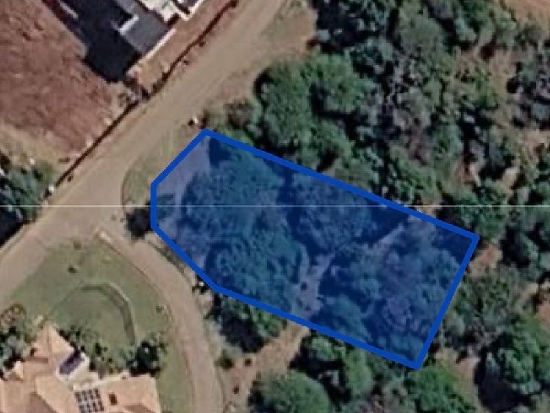 An aerial view of a vacant residential plot featuring established vegetation and surrounding neighborhood infrastructure.