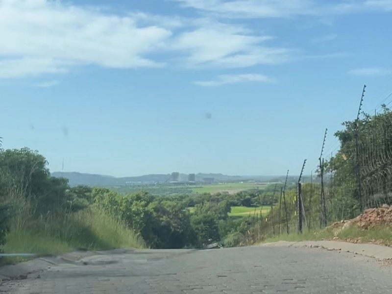 A view looking down a paved road towards a distant landscape with electric fencing along the perimeter.