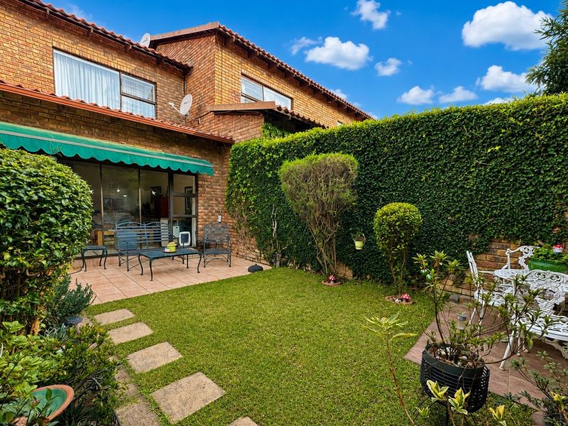 A private rear garden featuring a paved patio area, retractable awning, and established greenery, providing a pleasant outdoor space for relaxation.