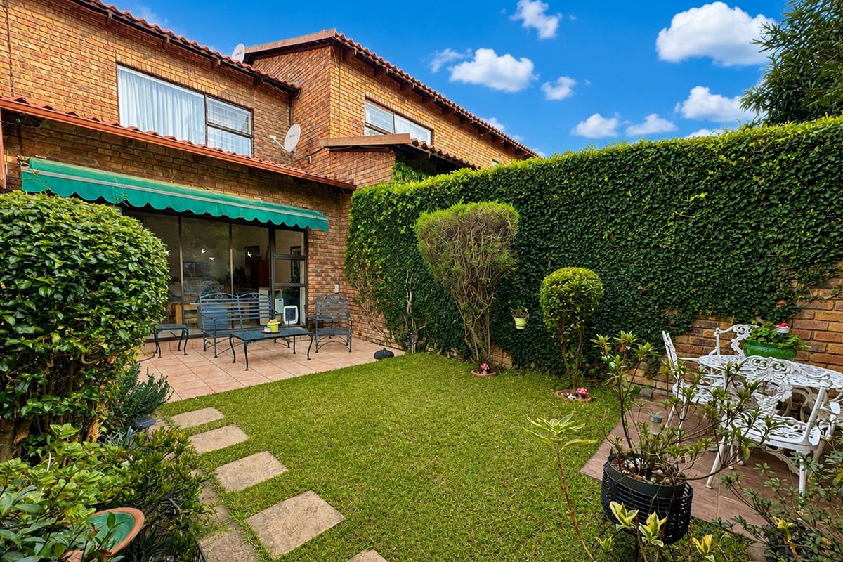 A private rear garden featuring a paved patio area, retractable awning, and established greenery, providing a pleasant outdoor space for relaxation.