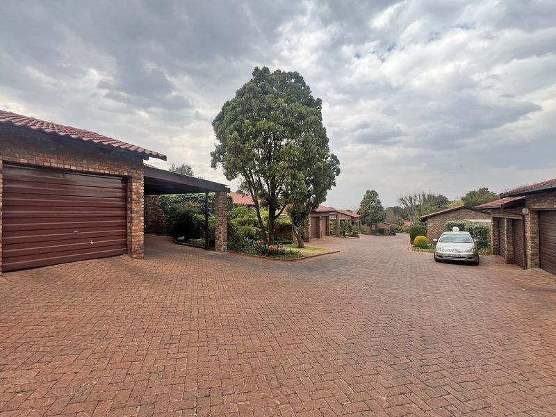 A view of the townhouse complex driveway featuring facebrick facades, tiled roofs, and paved access leading to multiple garage units.