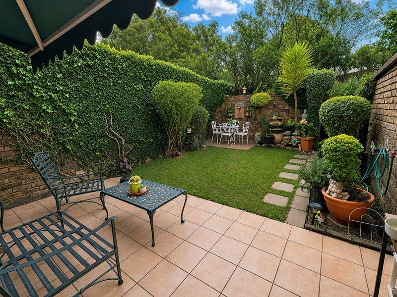 A well-maintained rear garden featuring a tiled patio with a retractable awning, lush lawn, and established brick boundary walls.