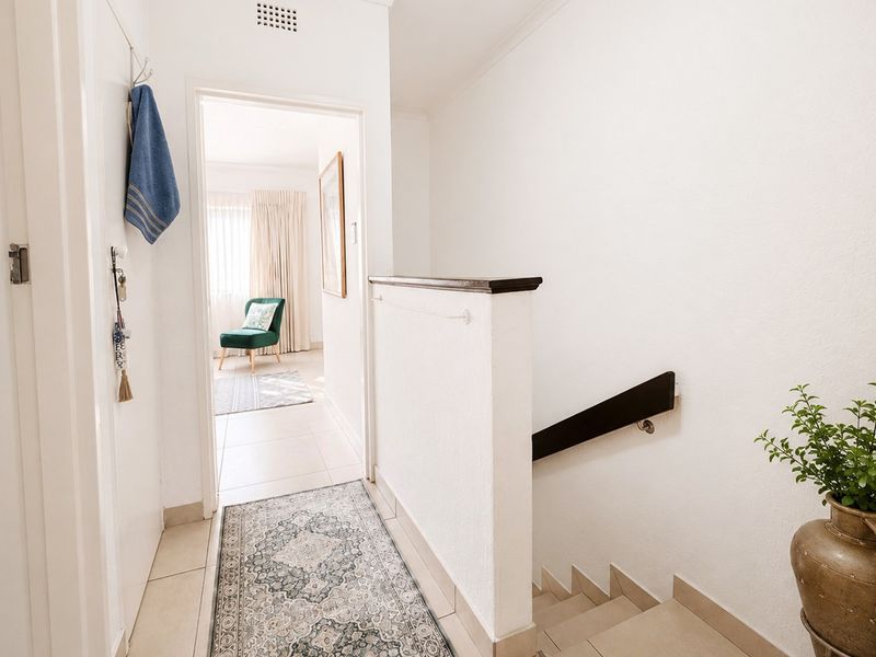 A bright upper-level hallway featuring tiled flooring, a staircase with a dark timber handrail, and access to adjacent living spaces.