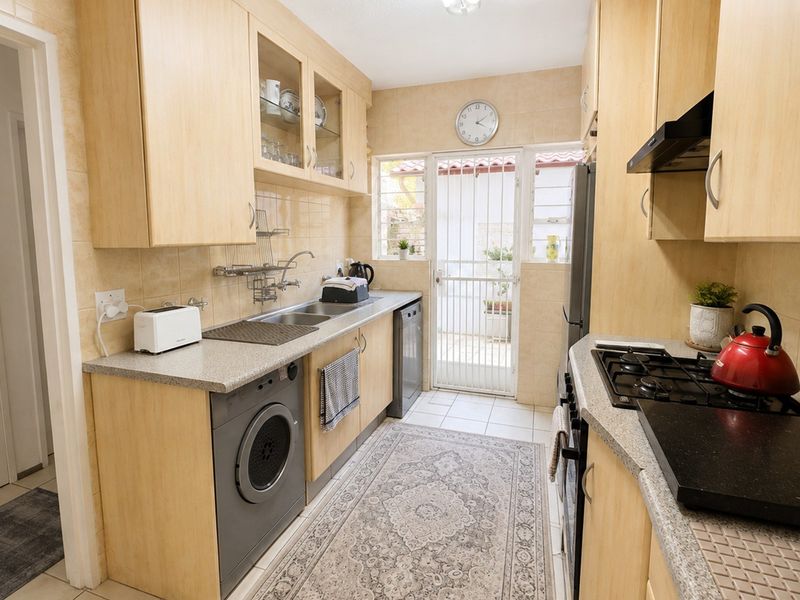 Functional galley-style kitchen featuring light wood cabinetry, gas hob, extractor fan, and direct access to an outdoor area through a security gate.