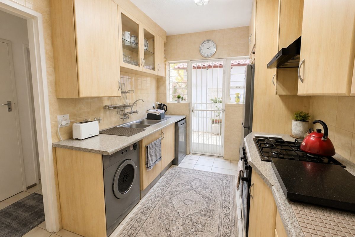 Functional galley-style kitchen featuring light wood cabinetry, gas hob, extractor fan, and direct access to an outdoor area through a security gate.