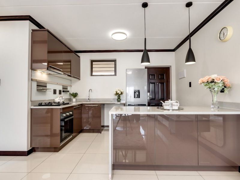 Modern kitchen featuring high-gloss brown cabinetry, stone countertops, integrated appliances, and stylish pendant lighting, finished with clean tiled flooring.