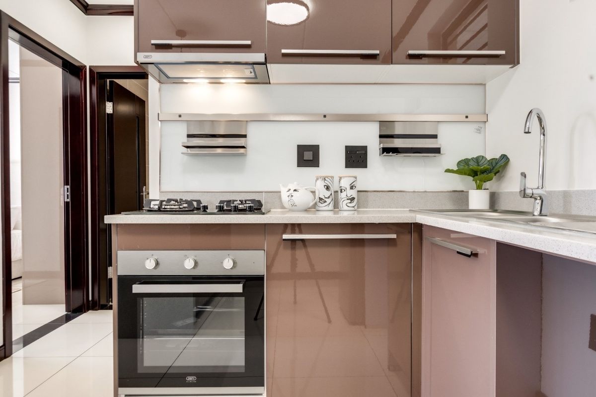 Modern kitchen featuring high-gloss brown cabinetry, stone countertops, built-in oven, gas hob, and a sleek glass splashback with integrated shelving.