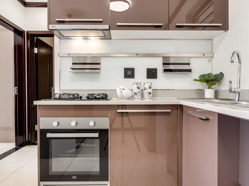Modern kitchen featuring high-gloss brown cabinetry, stone countertops, built-in oven, gas hob, and a sleek glass splashback with integrated shelving.