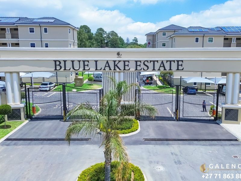 Aerial view of the main entrance gate and security access point for Blue Lake Estate, featuring paved driveway and modern apartment complex architecture.