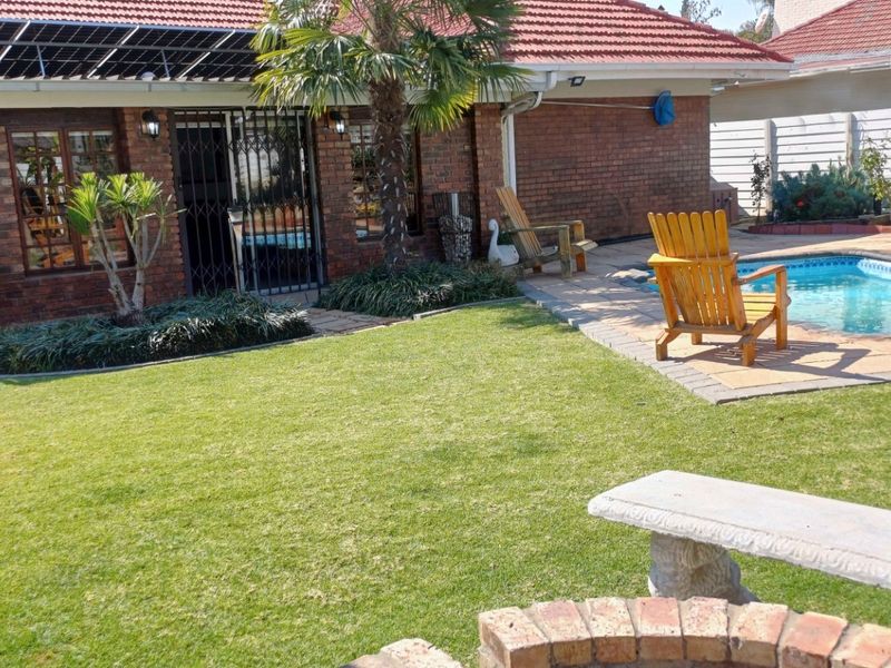 Rear garden area featuring a swimming pool, paved surround, and brick house exterior with installed solar panels.