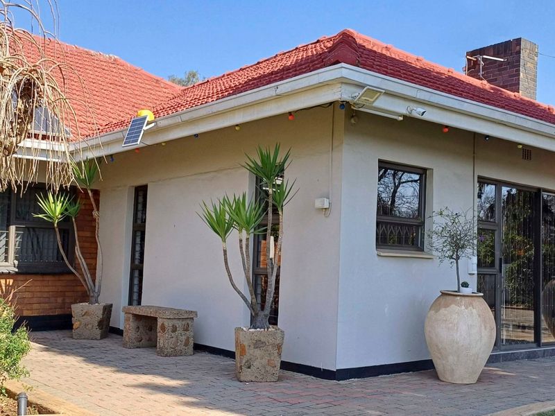A well-maintained rear exterior view featuring a terracotta tiled roof, paved patio area, and sliding glass doors with security bars.