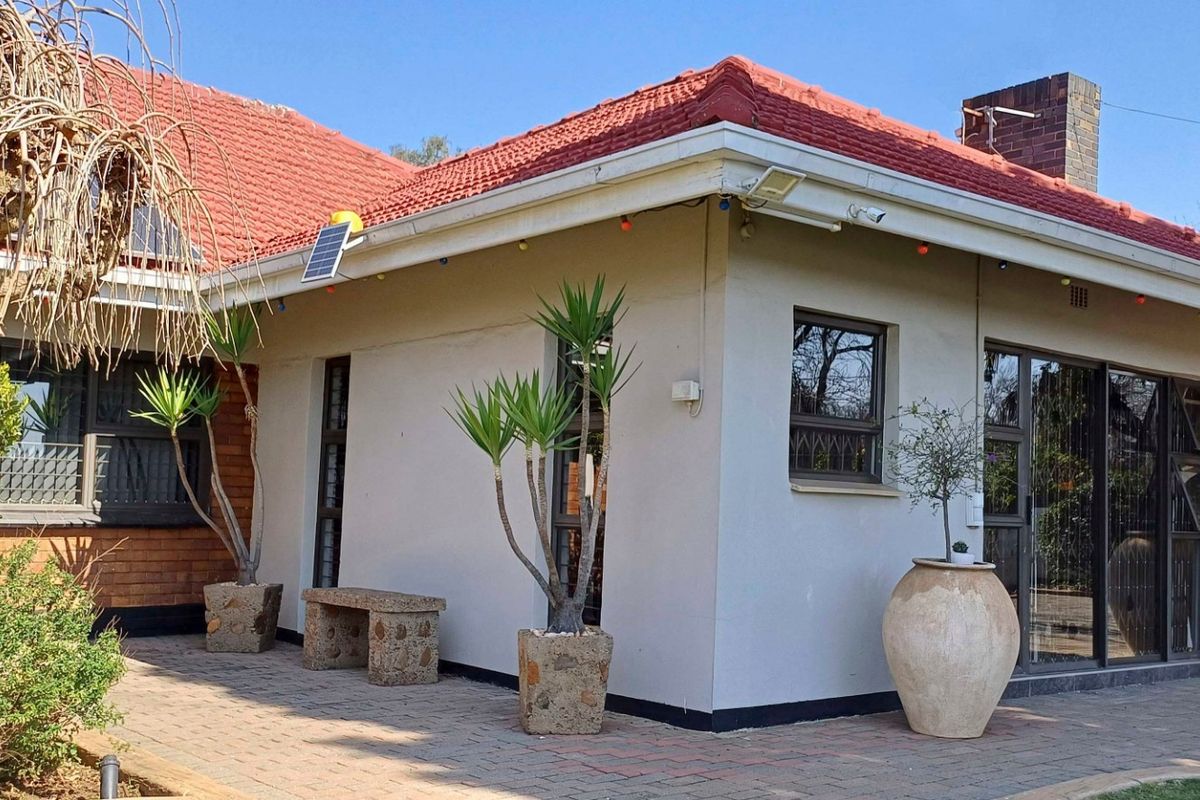 A well-maintained rear exterior view featuring a terracotta tiled roof, paved patio area, and sliding glass doors with security bars.