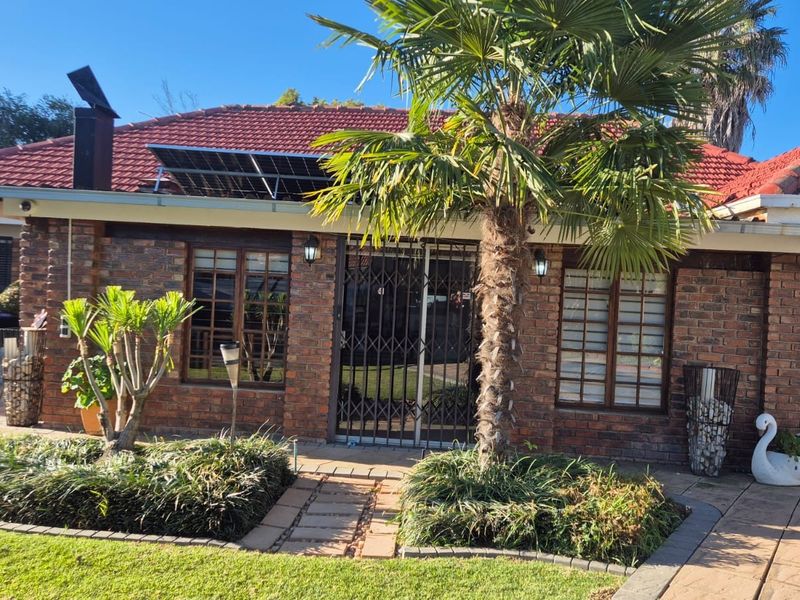 Front elevation of a face brick house featuring a tiled roof, solar panels, security gate entrance, and a well-maintained landscaped garden with paved walkway.