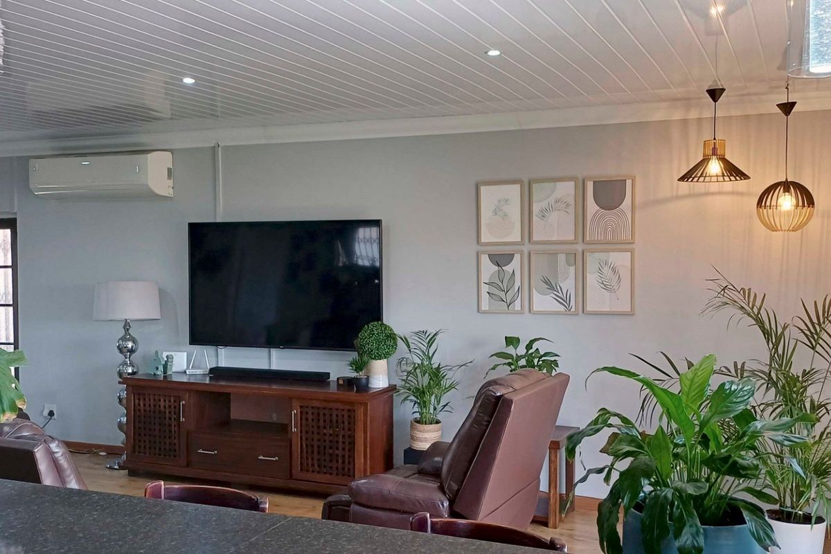 A comfortable living room featuring a split-system air conditioner, recessed downlights, modern pendant lighting, and a clean tongue and groove ceiling finish.