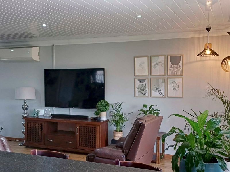 A comfortable living room featuring a split-system air conditioner, recessed downlights, modern pendant lighting, and a clean tongue and groove ceiling finish.