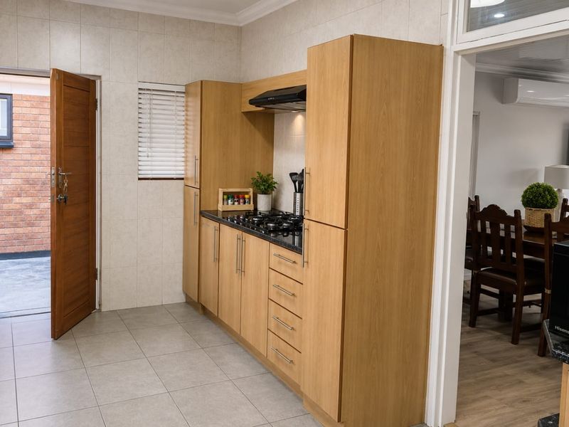 A well-maintained kitchen featuring light wood cabinetry, a gas hob with extractor fan, tiled flooring, and direct access to an exterior courtyard.