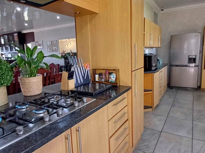 A functional kitchen featuring wooden cabinetry, granite countertops, a gas hob with extractor, and a built-in oven, with tiled flooring throughout.