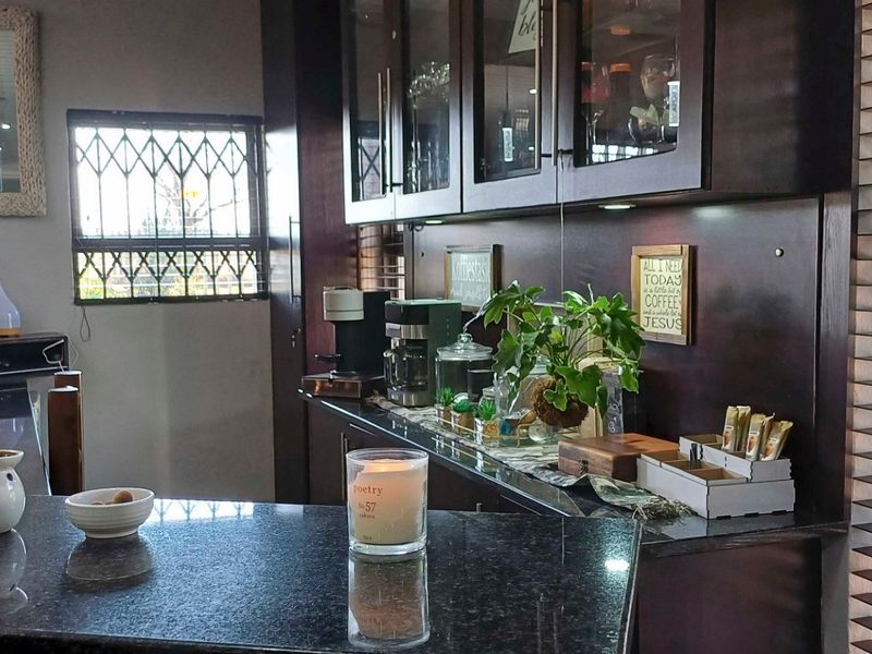 A well-maintained kitchen featuring dark wood cabinetry, granite countertops, and large windows with security bars and venetian blinds.