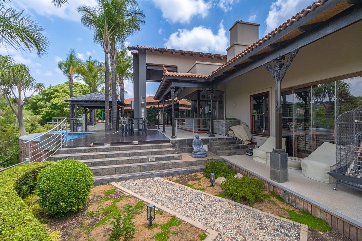 Spacious rear exterior featuring a covered patio, timber decking, swimming pool, and landscaped garden with a stone pathway.