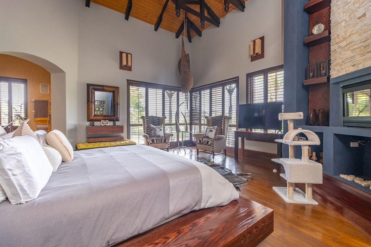 Spacious bedroom featuring a vaulted timber ceiling with exposed beams, hardwood flooring, and a prominent stone-clad fireplace.